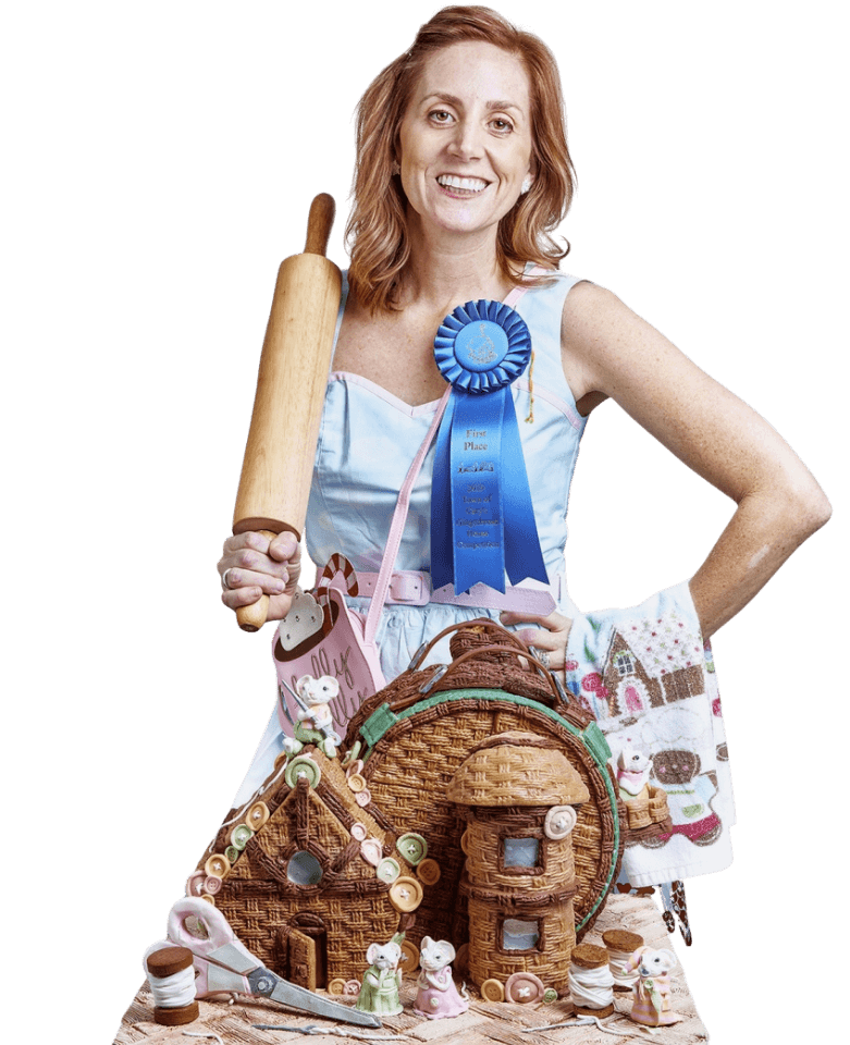Baker holding rolling pin beside decorated gingerbread cottage